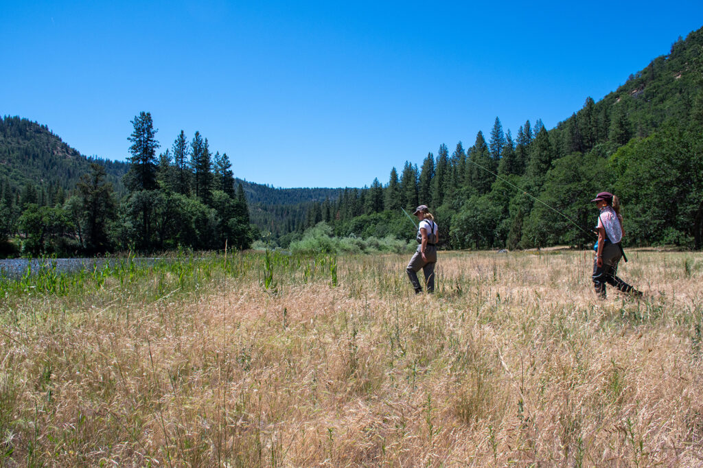 two young women angler hiking to stream