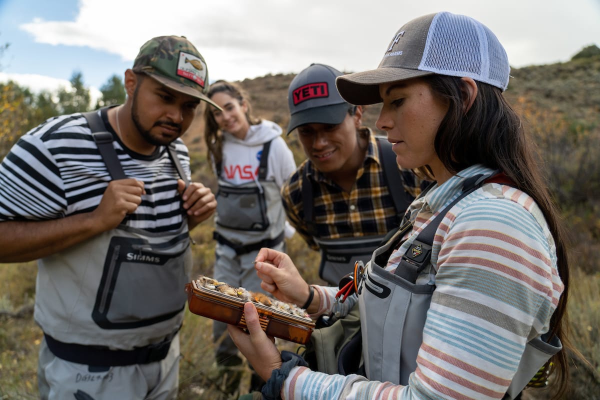 woman holding fly box giving fly fishing tips to small group